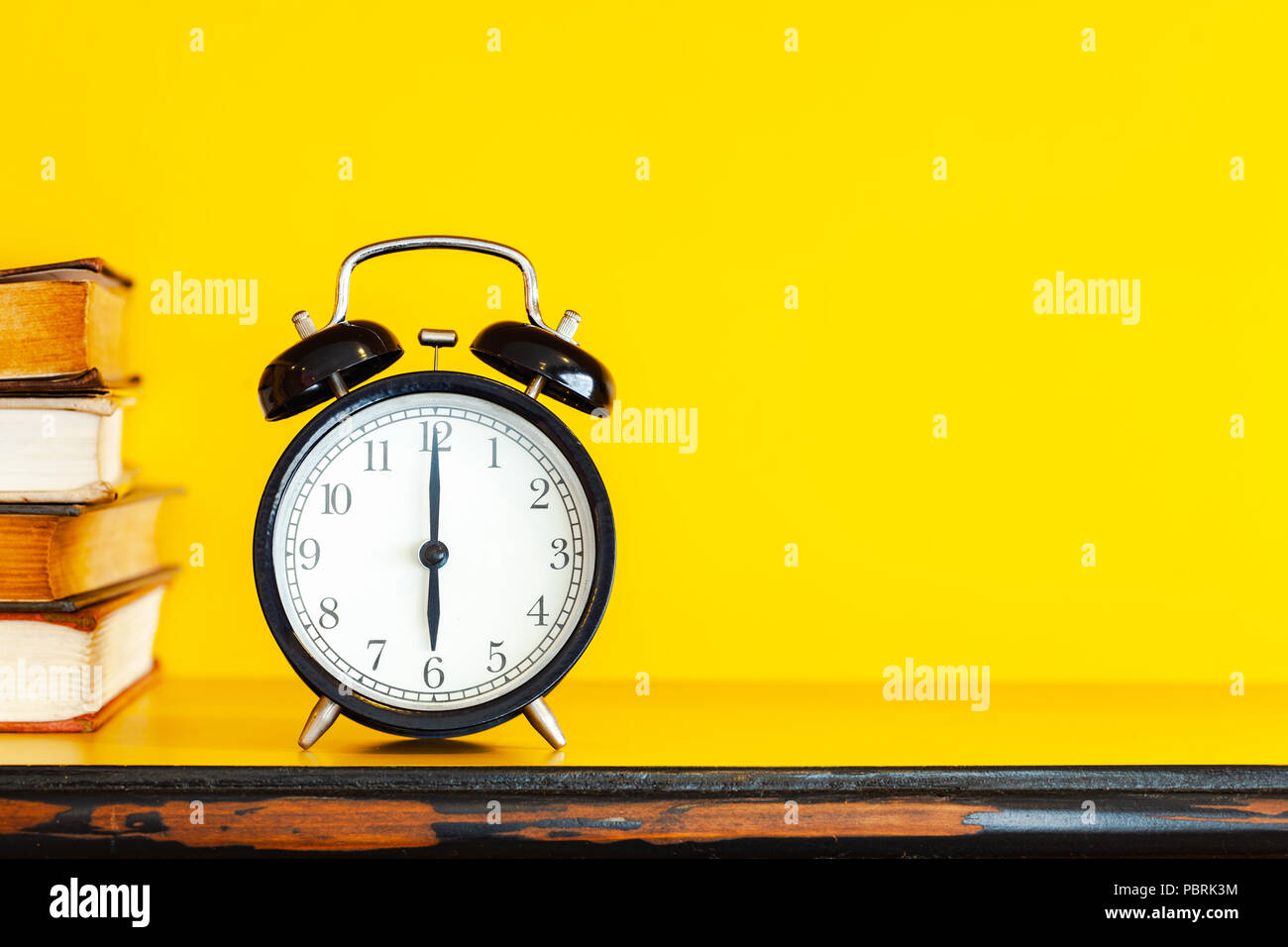 Alarm clock and book on yellow background with copy space. Stock Photo