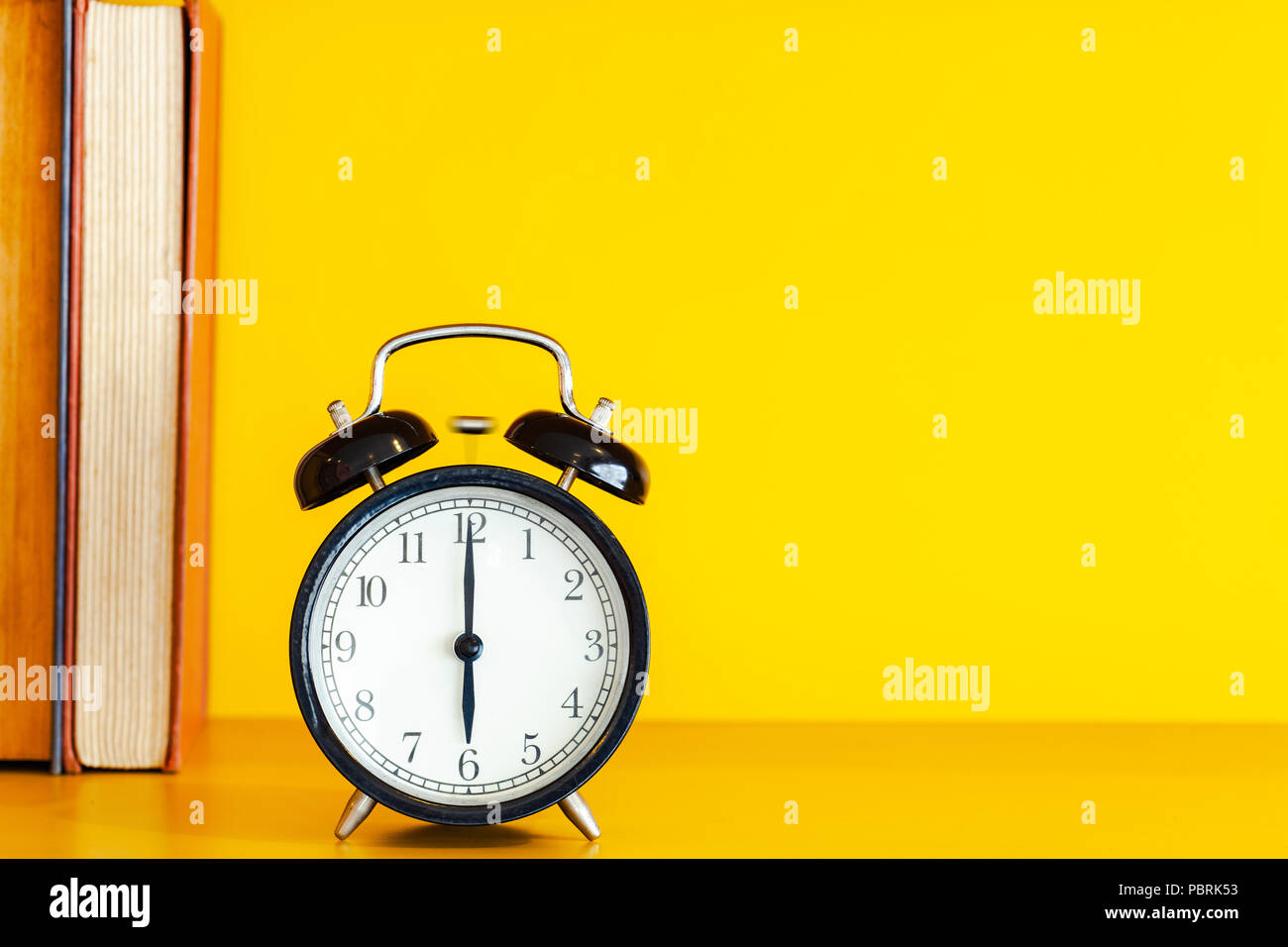 Alarm clock and book on yellow background with copy space. Stock Photo