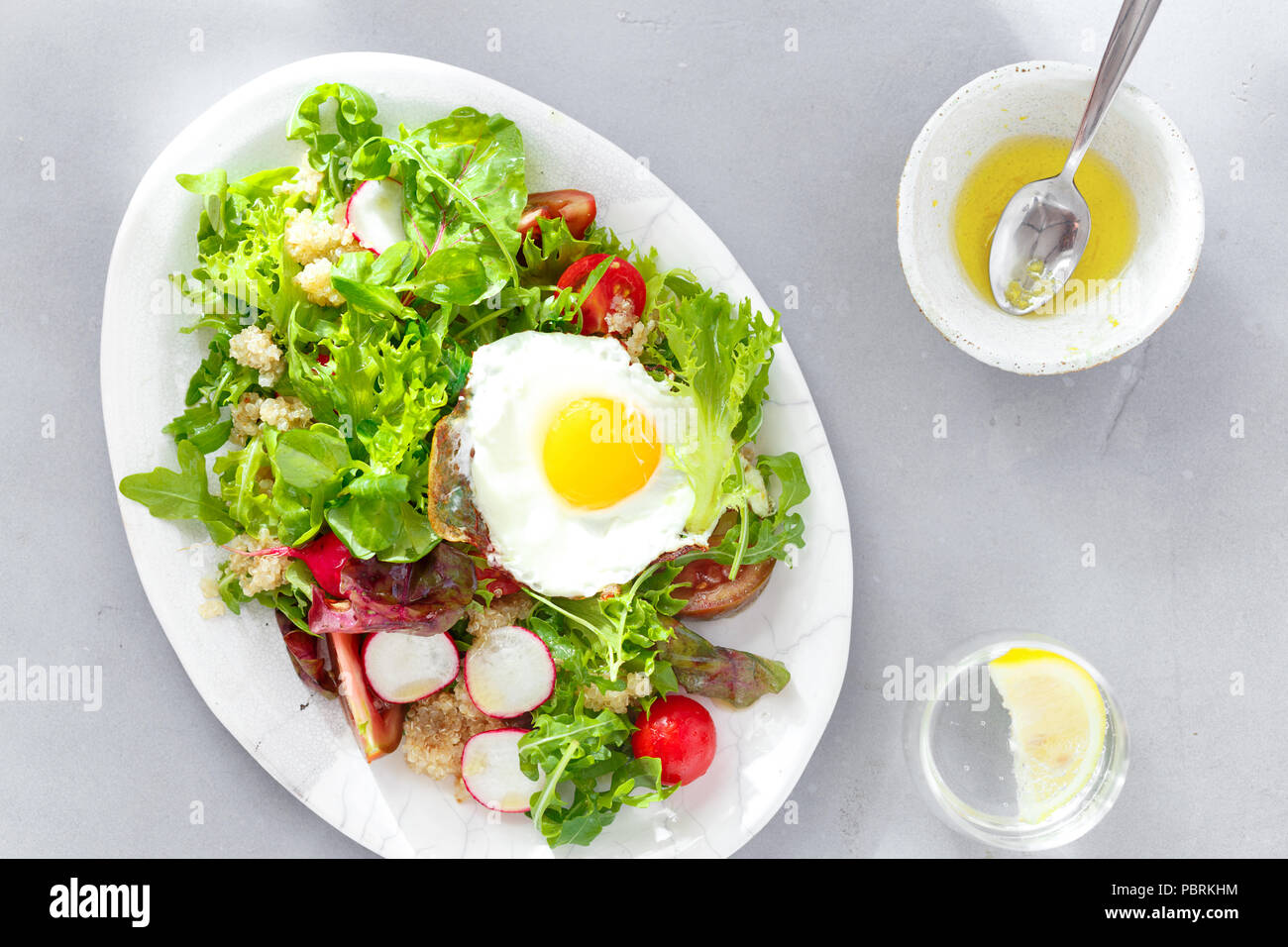 Plate fresh salad with quinoa, sauce, fried egg and glass lemon water on gray concrete background top view. Healthy food clean eating Stock Photo