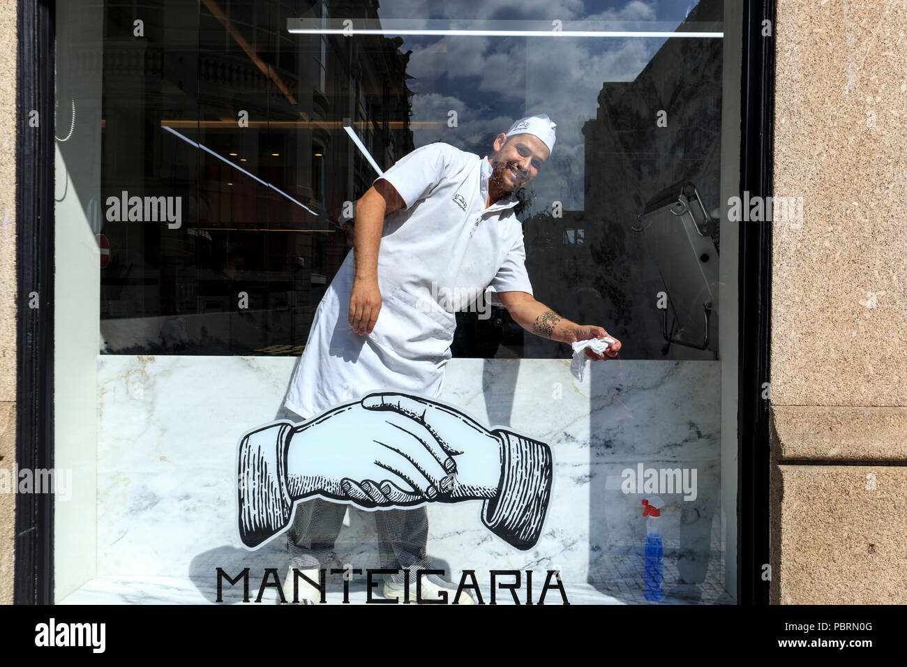A smiling man in chef clothing cleaning the inside of the window of the Manteigaria pastel de nata shop in Porto Portugal Stock Photo