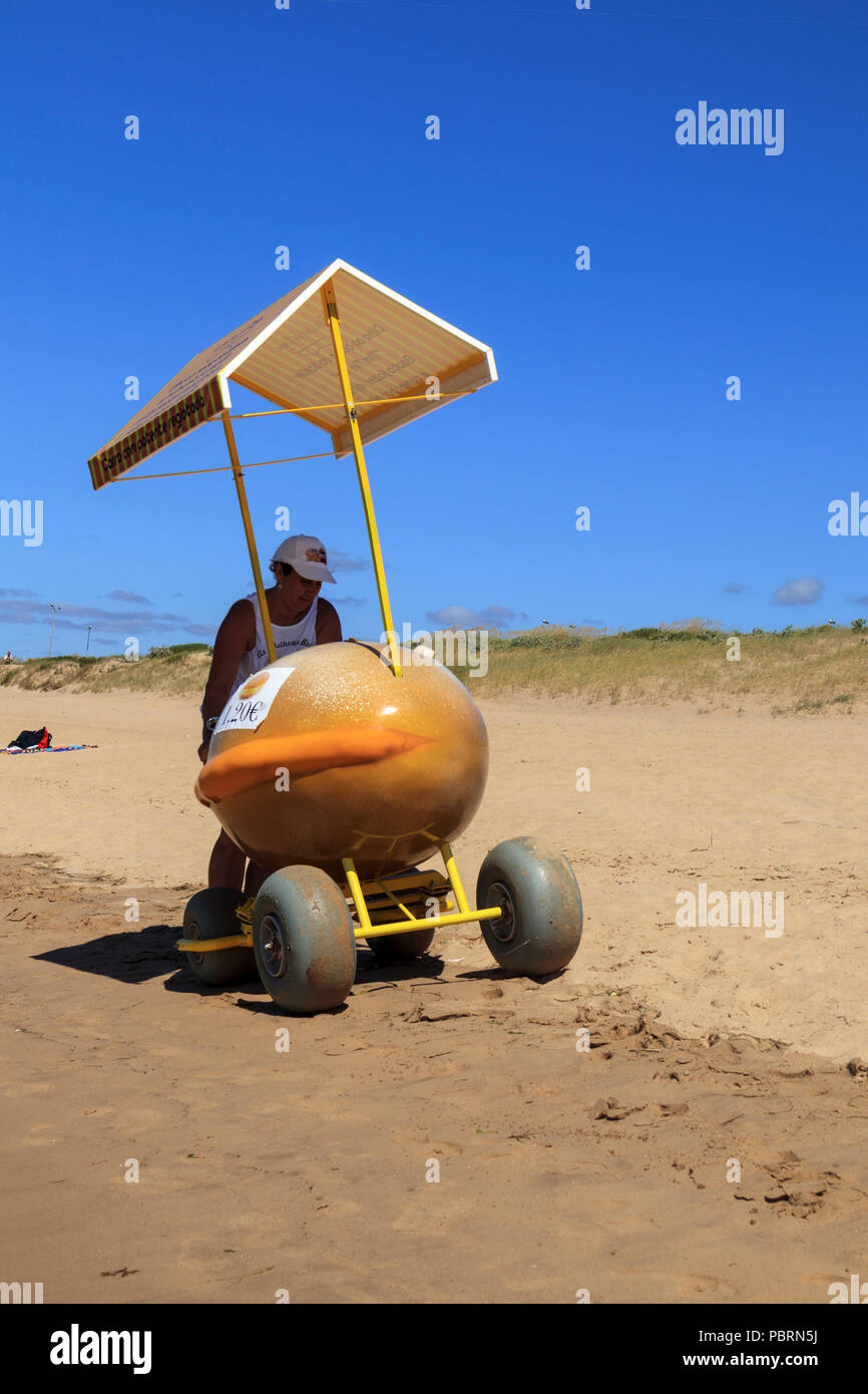 Doughnut seller pushing a doughnut shaped food cart with large wheels along the beach on a sunny day in Sao Martinho Portugal Stock Photo