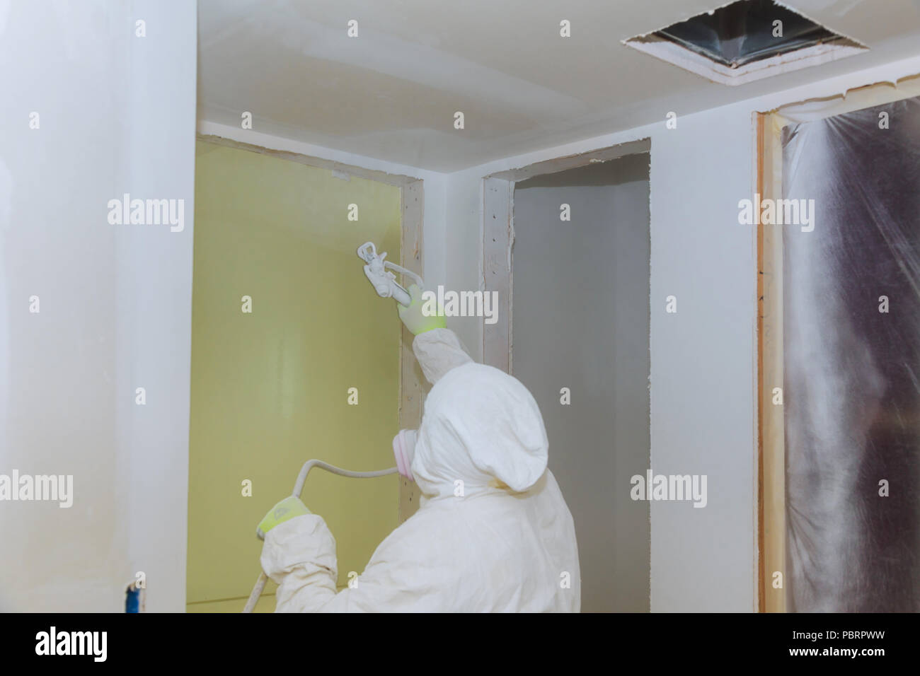 Man painting walls with white colour using spray paint gun hand the