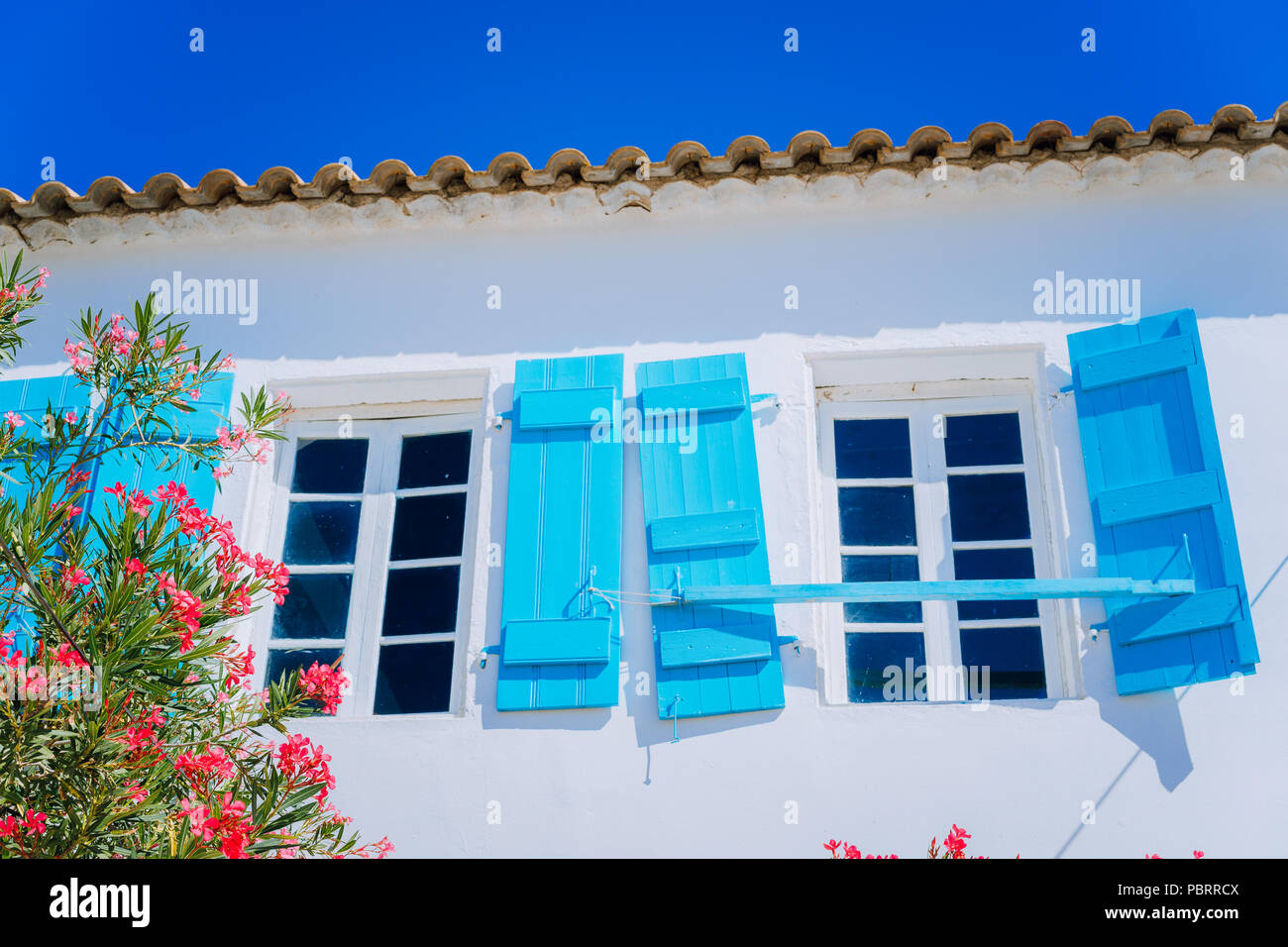 Traditional greek white house with blue window shutter and flowers in