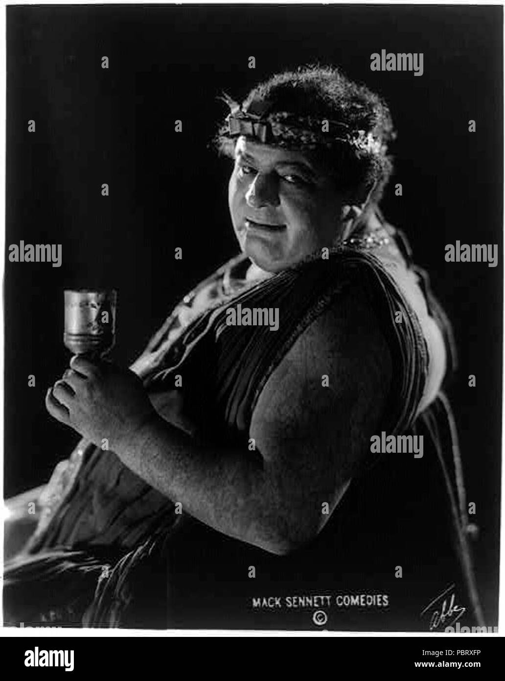 Actor from Mack Sennett comedy film in Roman toga seated holding wine glass) - Abbe Stock Photo