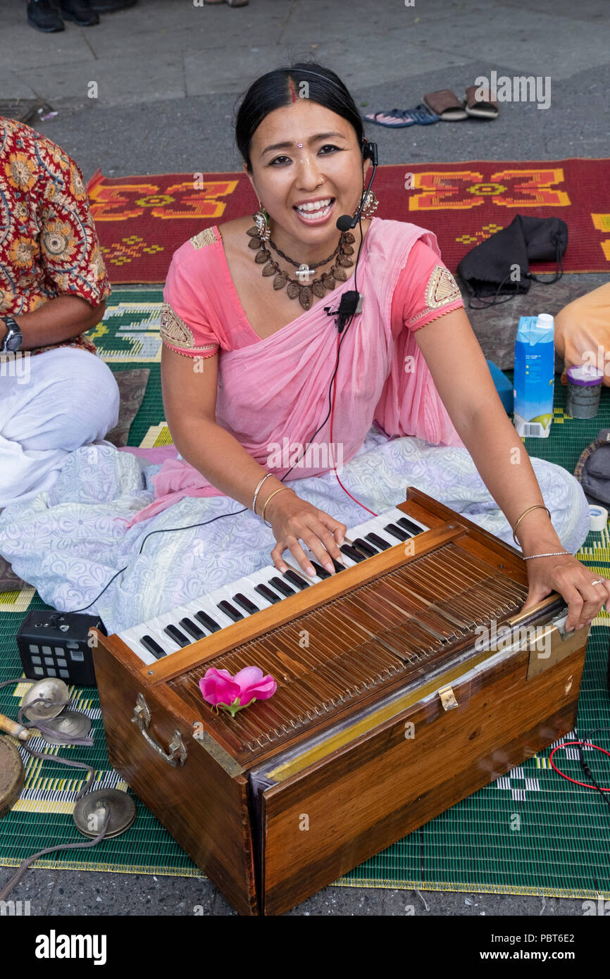 An attractive Japanese Hare Krishna devotee chants and plays the harmonium in Union Square Park in Manhattan, New York City Stock Photo