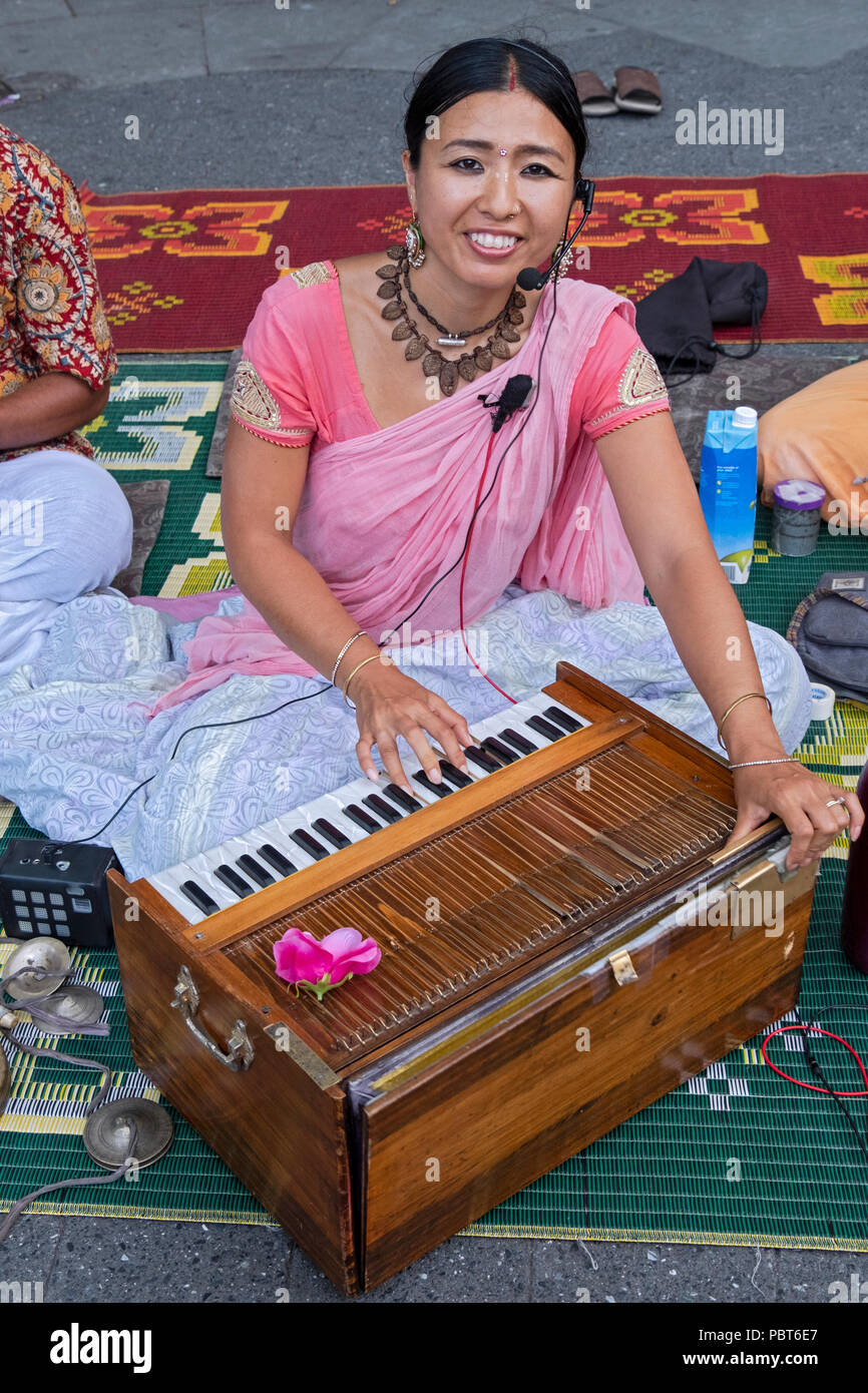 An attractive Japanese Hare Krishna devotee chants and plays the harmonium in Union Square Park in Manhattan, New York City Stock Photo