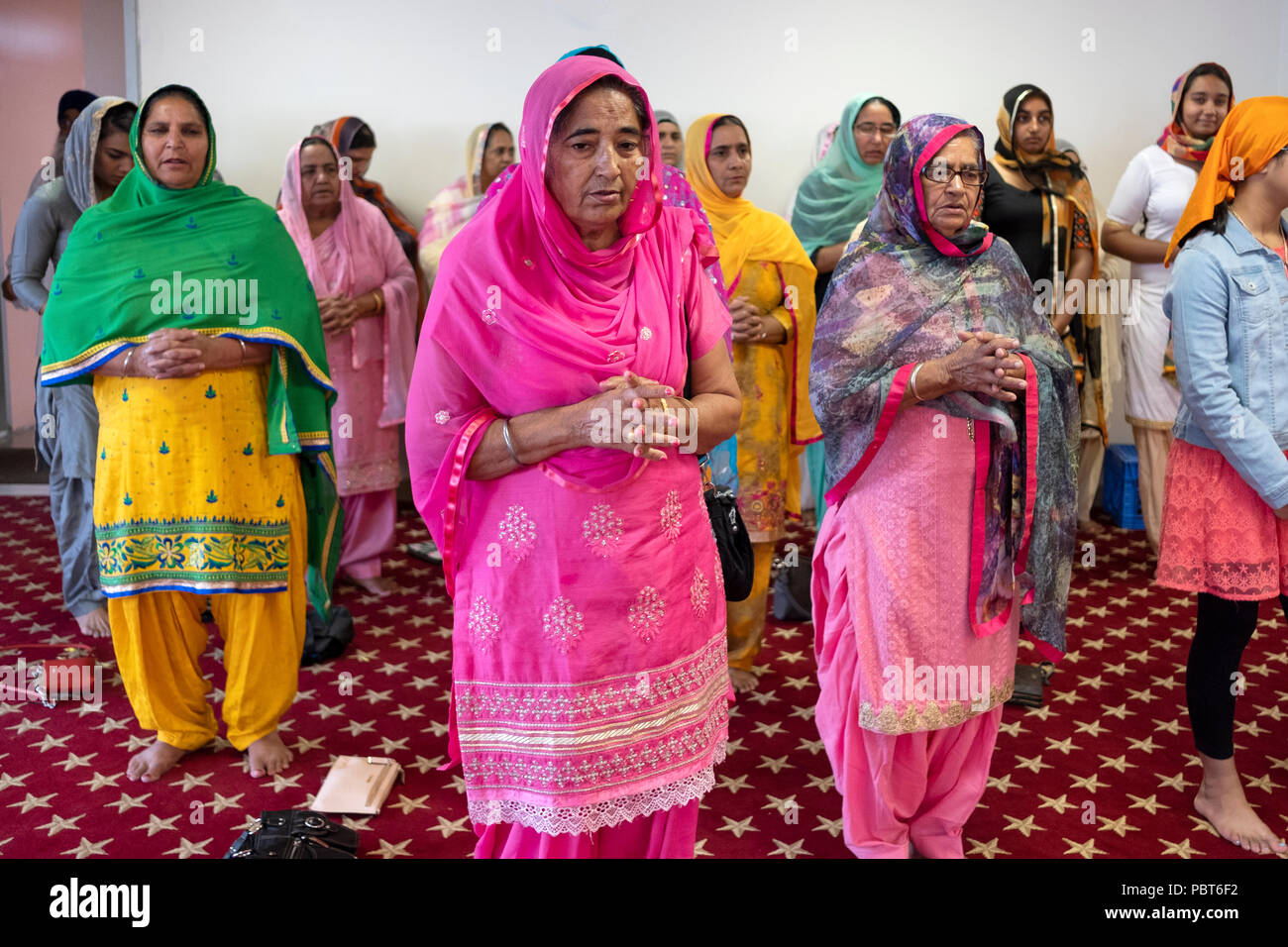 Women, mostly older, stand with clasped hands praying and meditating at a temple in South Richmond Hill, New York. Stock Photo