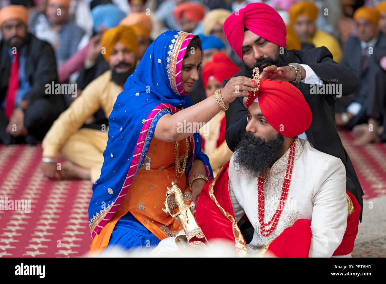 Guests at a Sikh wedding in Richmond Hill, Queens, New York adjust the pin on the groom's turban. Stock Photo