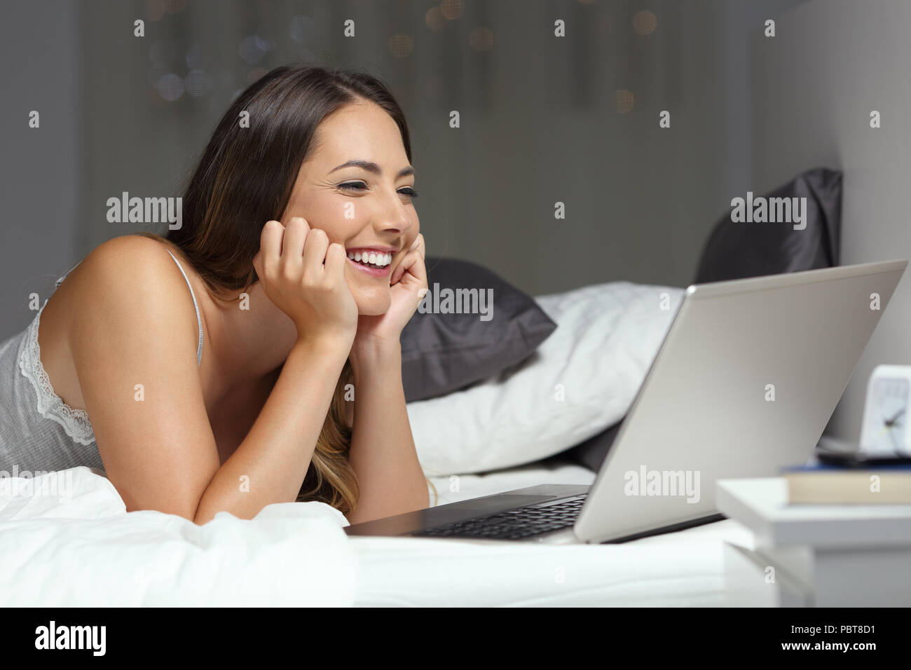 Candid woman using a laptop on a bed in the night at home Stock Photo
