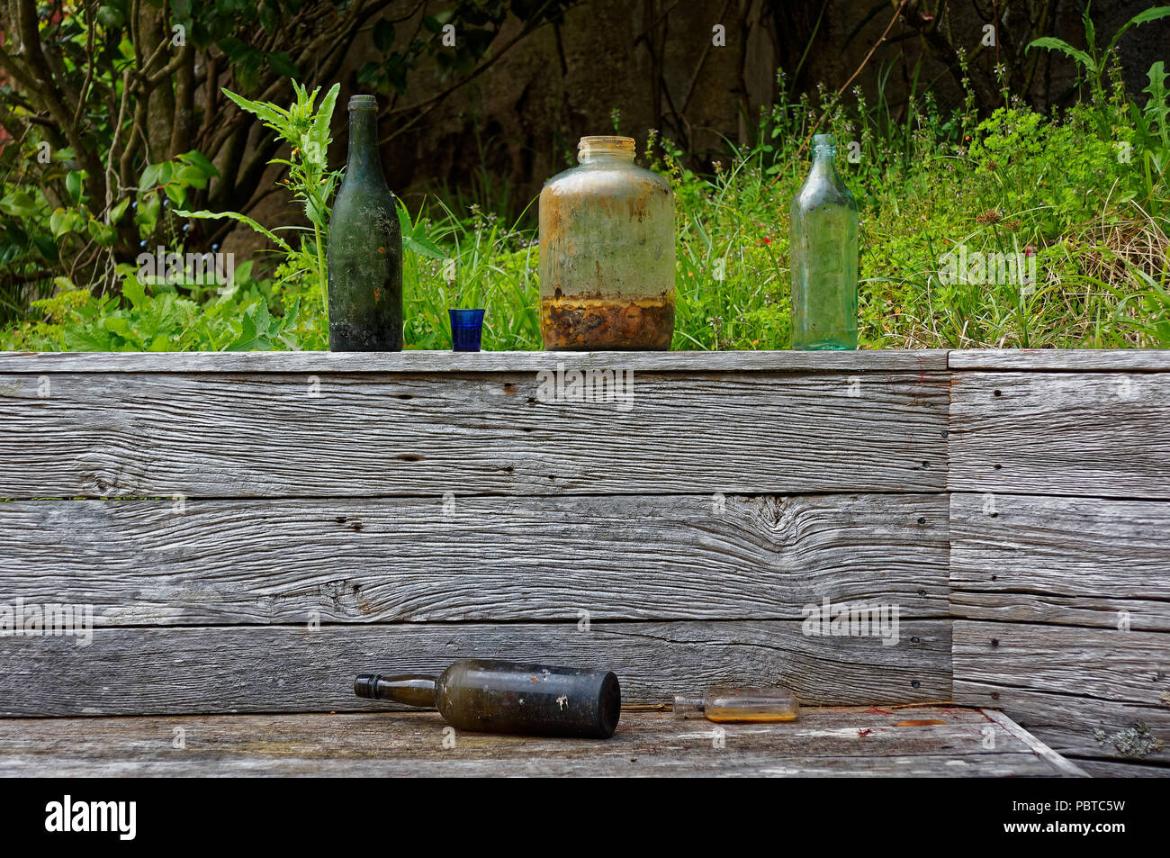 Old bottles and jars discarded on a wooden garden fence Stock Photo