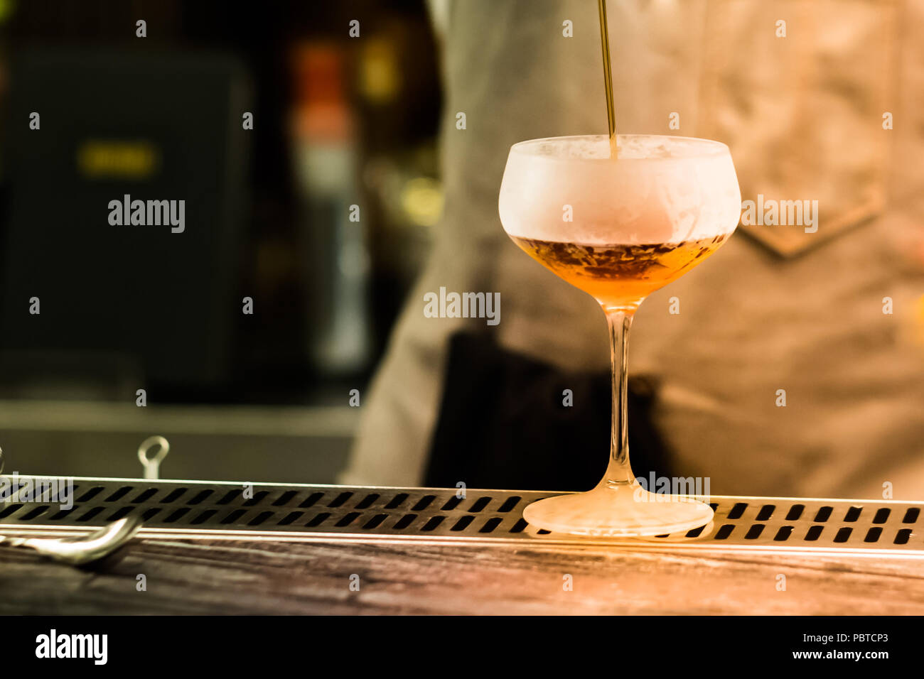 Professional bartender pouring cocktail from shaker into the glass