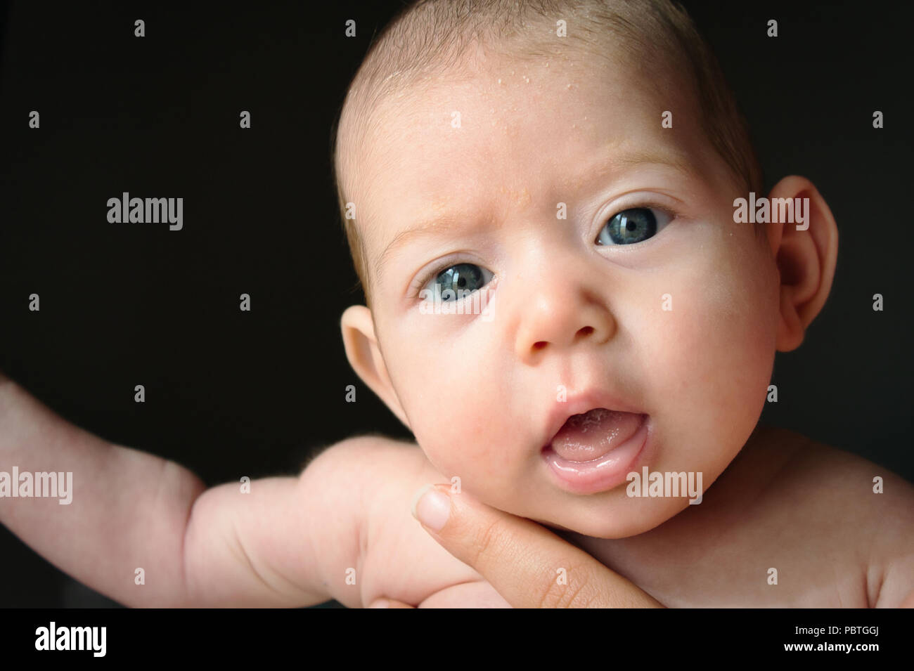 Newborn baby against black background with big eyes looking into the