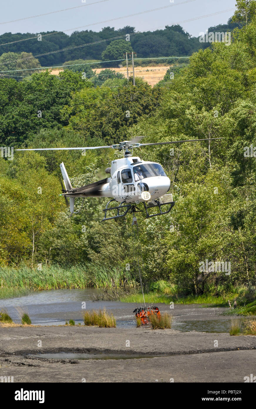 A helicopter hovering over a pond to fill a large water bucket before