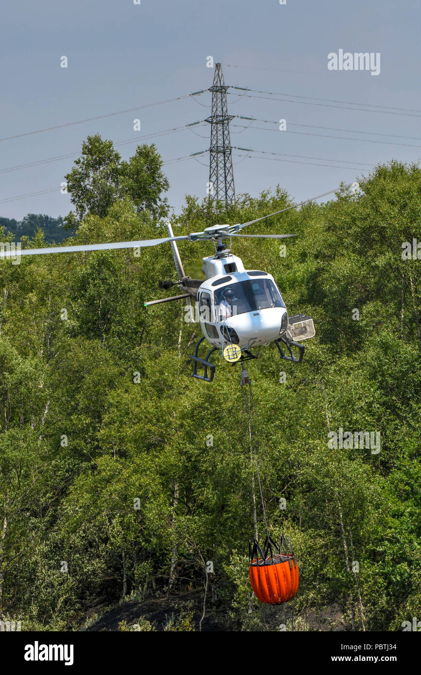 A helicopter taking off with a large bucket of water. The helicopter is