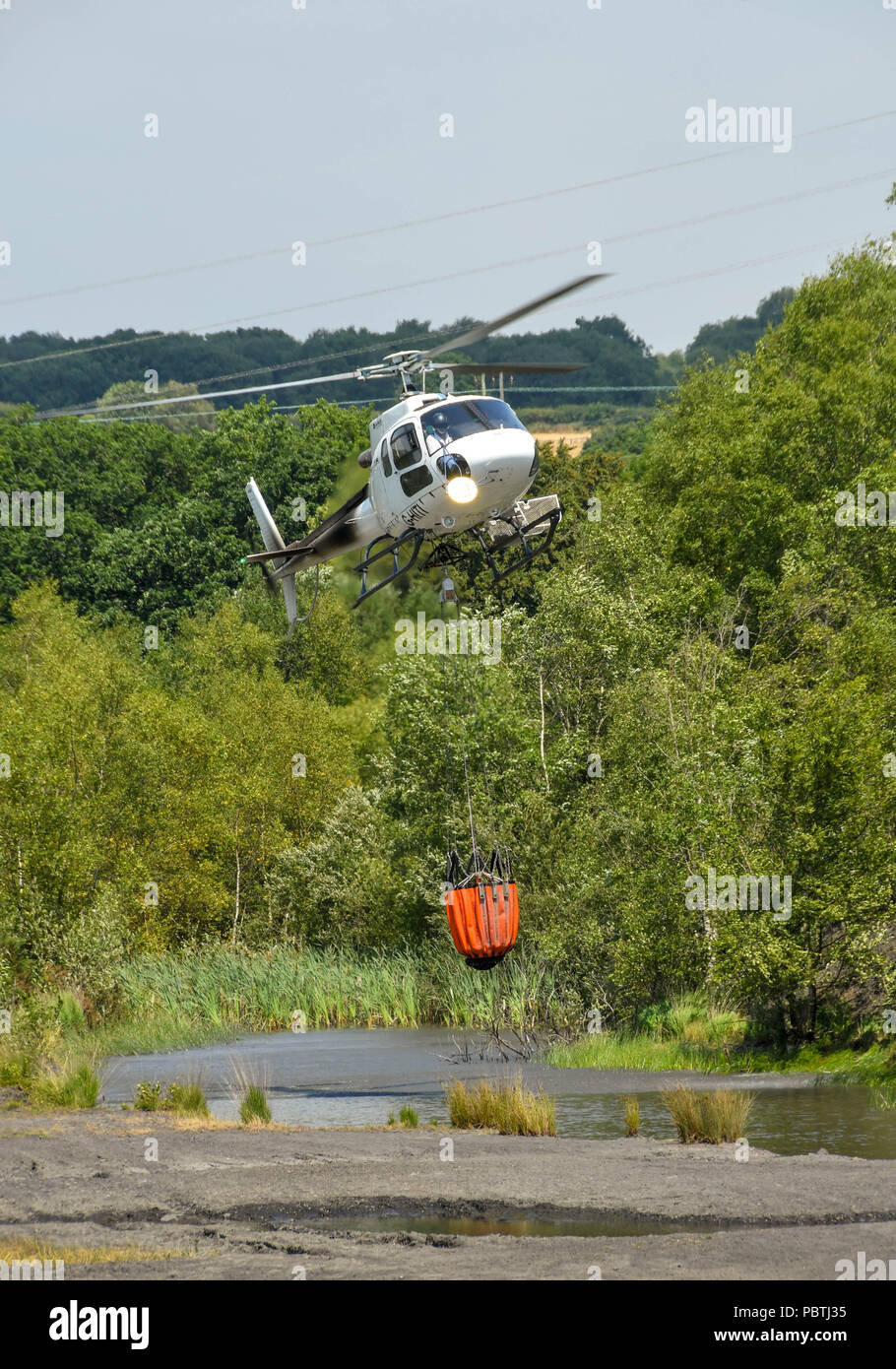 A helicopter hovering over a pond to fill a large water bucket before