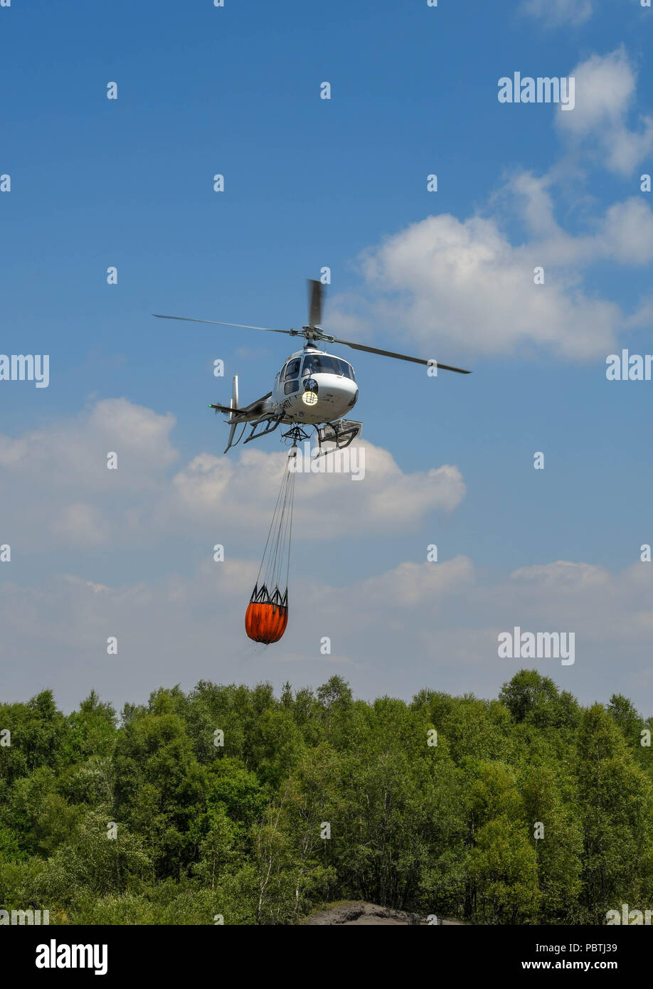 A helicopter taking off with a large bucket of water. The helicopter is
