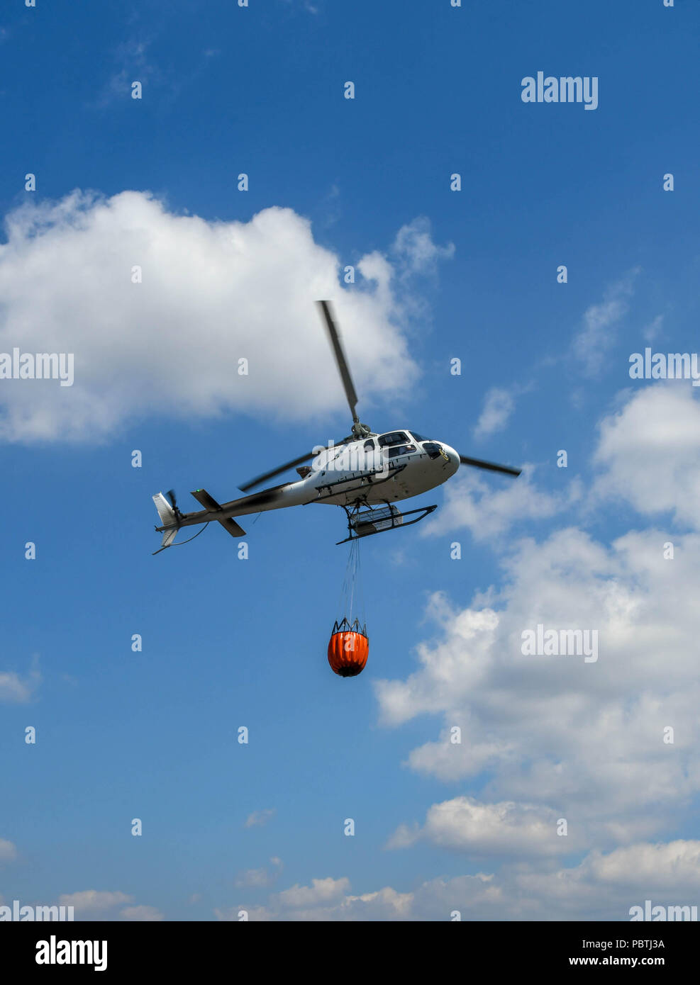 A helicopter carrying a large bucket of water. The helicopter is being