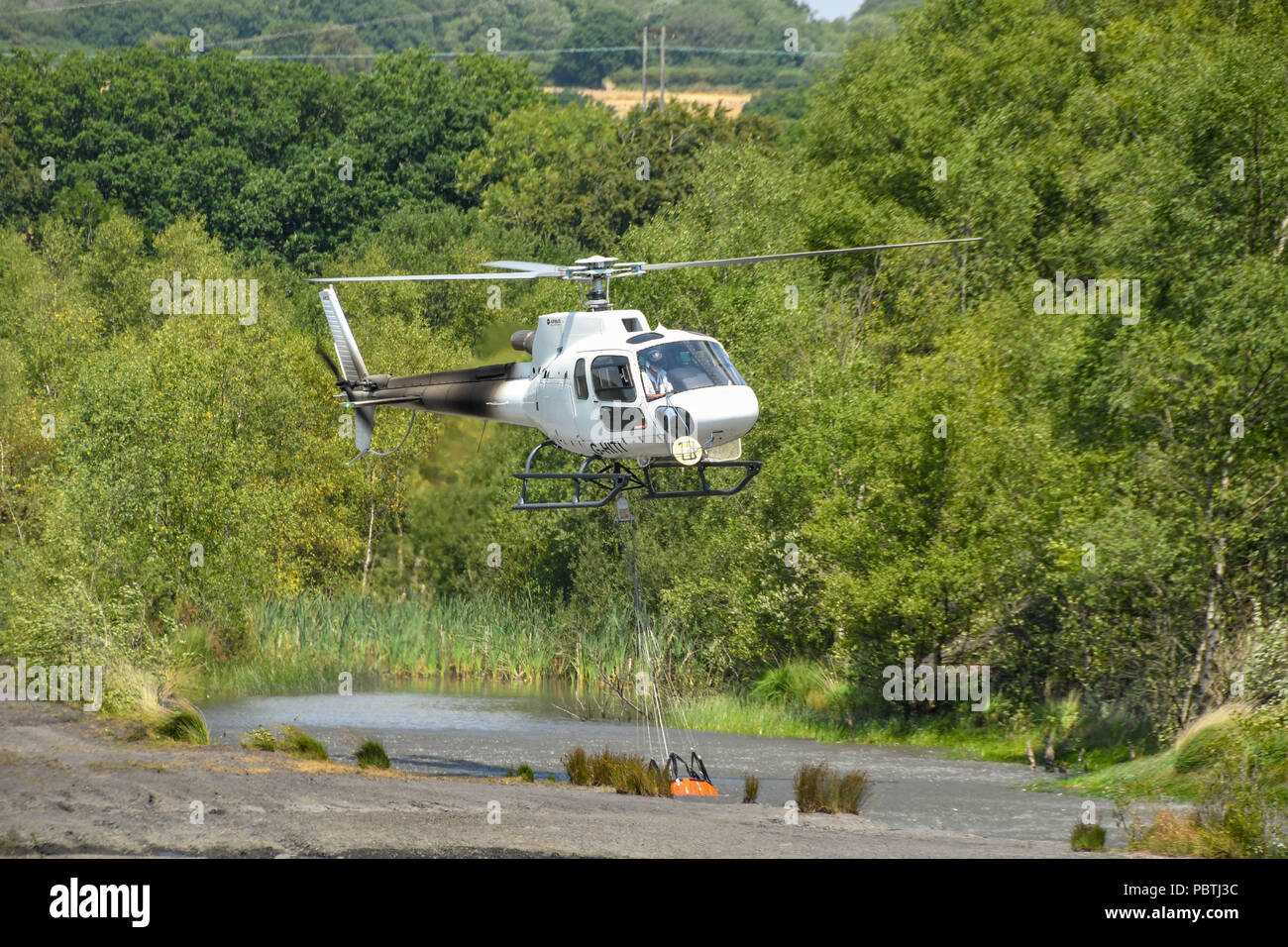 A helicopter hovering over a pond to fill a large water bucket before