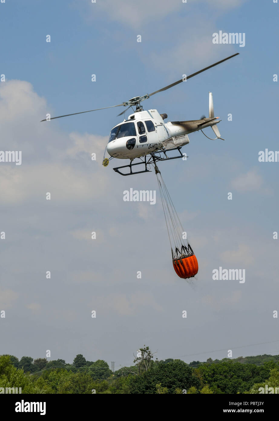 A helicopter carrying a large bucket of water. The helicopter is being