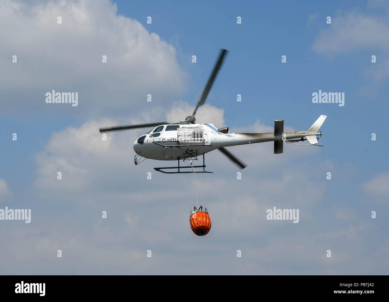 A helicopter carrying a large bucket of water. The helicopter is being