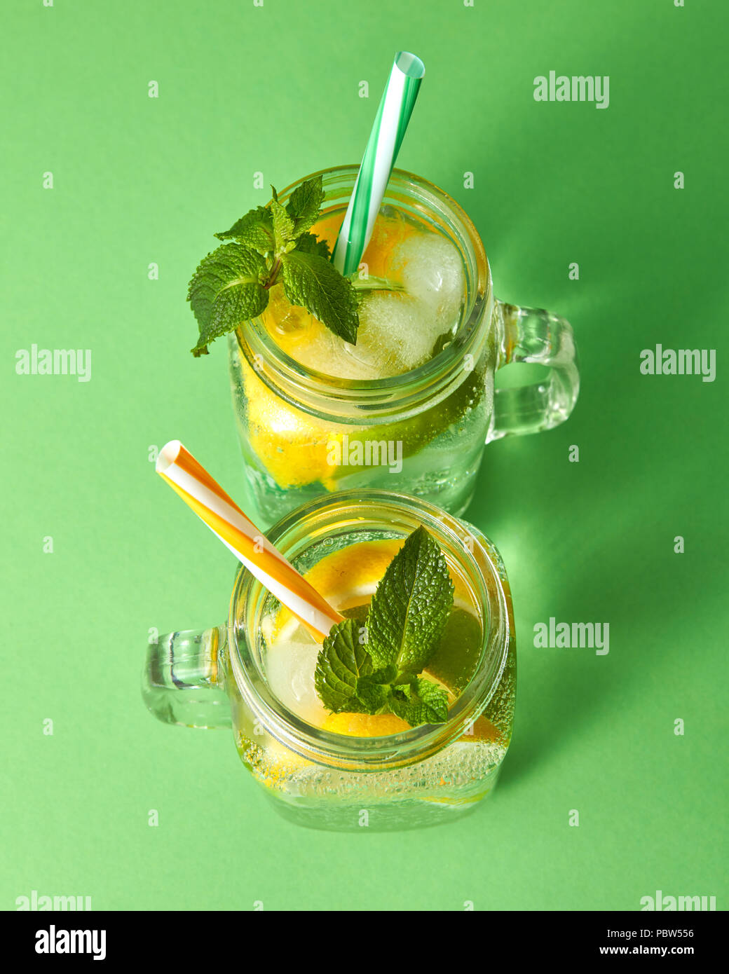 https://c8.alamy.com/comp/PBW556/citrus-fruits-slices-of-lemon-and-lime-ice-water-and-plastic-straws-in-the-glass-on-a-green-background-two-glass-jars-with-a-cold-natural-handmade-lemonade-with-bubbles-of-air-top-view-PBW556.jpg