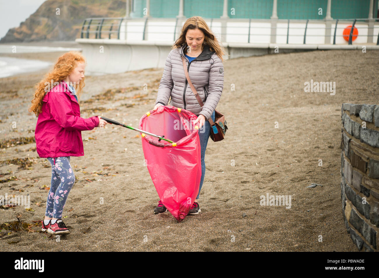 A woman and her daughter picking up litter off the beach in Aberystwyth WalesUK on a volunteering 'clean up' day, July 2018. Stock Photo