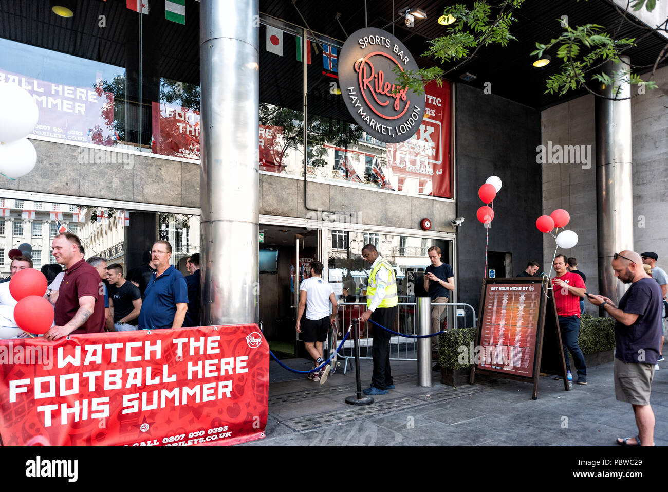 London, UK - June 24, 2018: People men lined up in line queue standing waiting by sidewalk street in England, by Riley's Sports Bar pub for watching F Stock Photo