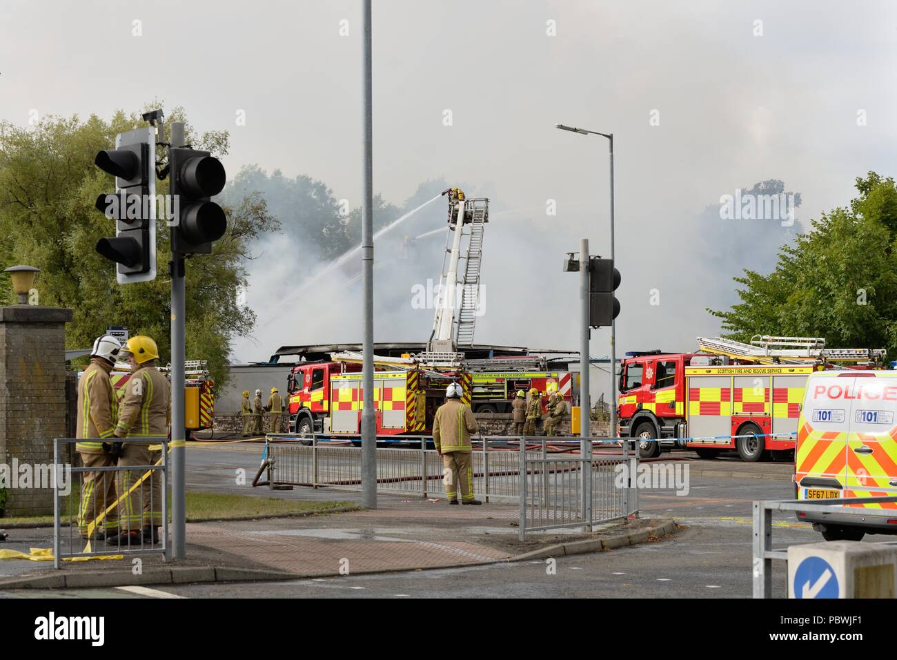 Glasgow, UK. 30th July, 2018. Glasgow, Scotland, UK. A large fire forces the closure of Crookston Rd in Glasgow as fire appliances line the street and firefighters use breathing apparatus and high reach platforms to tackle the blaze. Credit: Douglas Carr/Alamy Live News Stock Photo