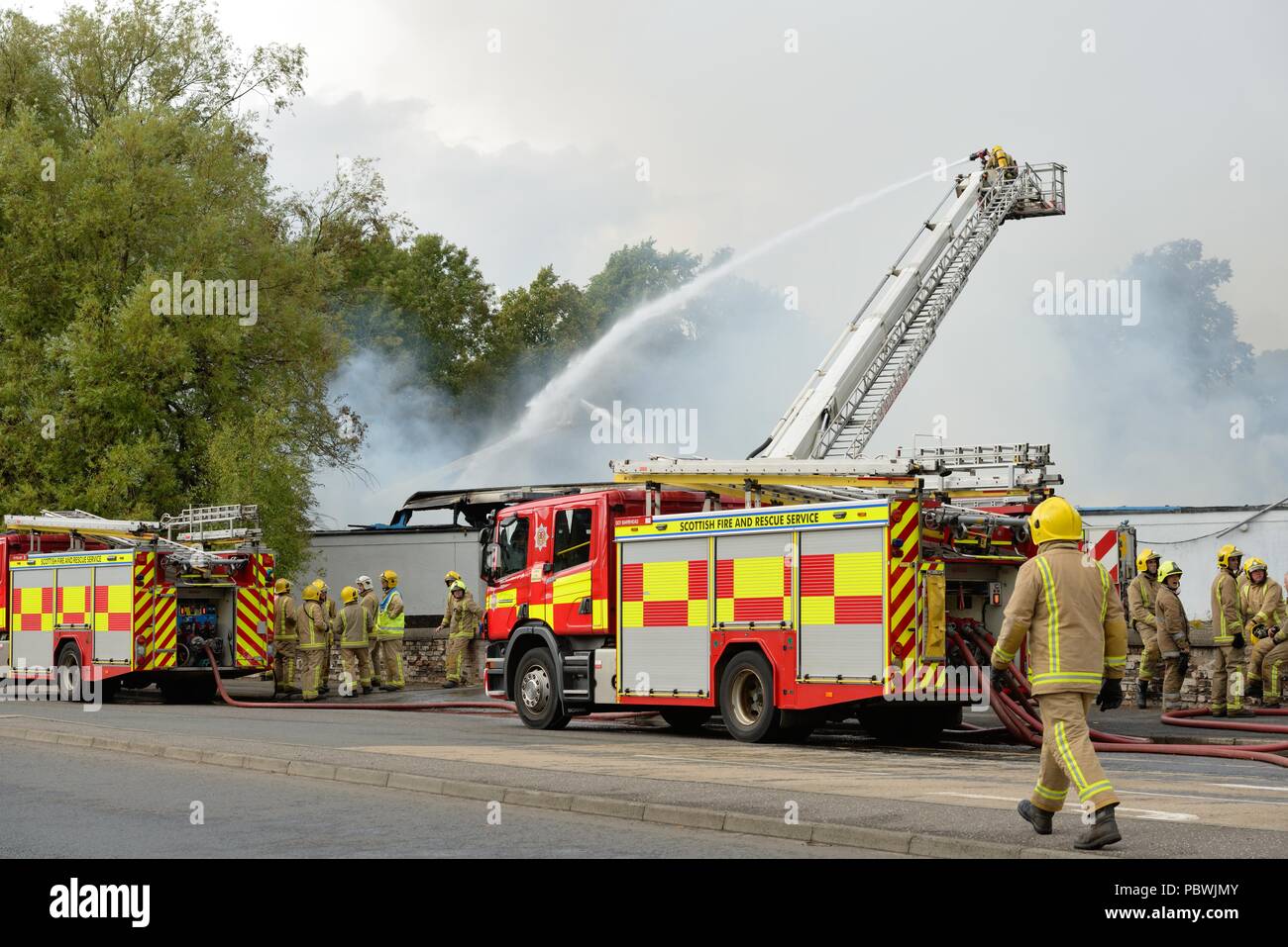 Glasgow, UK. 30th July, 2018. Glasgow, Scotland, UK. A large fire forces the closure of Crookston Rd in Glasgow as fire appliances line the street and firefighters use breathing apparatus and high reach platforms to tackle the blaze. Credit: Douglas Carr/Alamy Live News Stock Photo