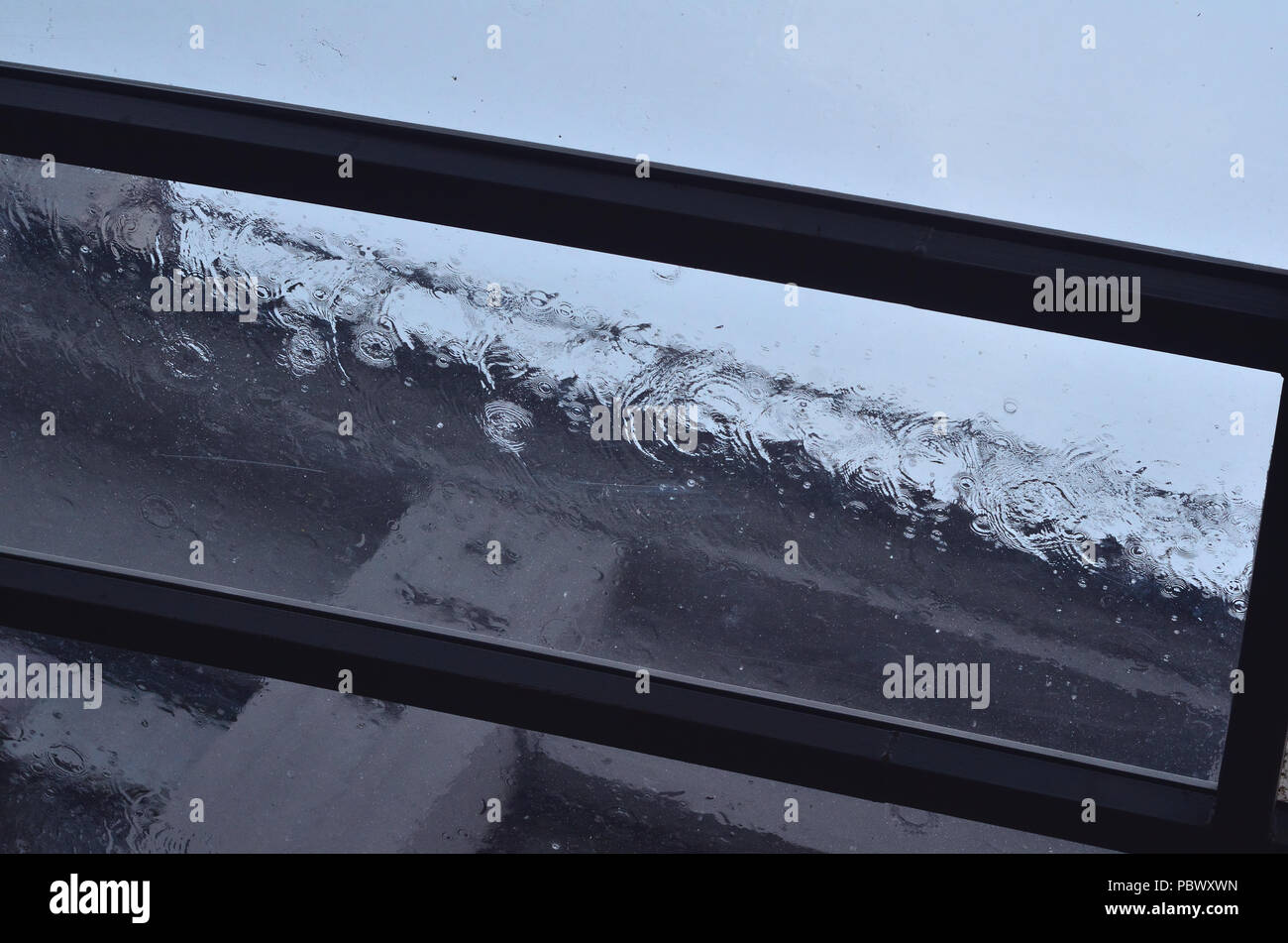 Strong rain pours on a glass roof during daylight hours Stock Photo