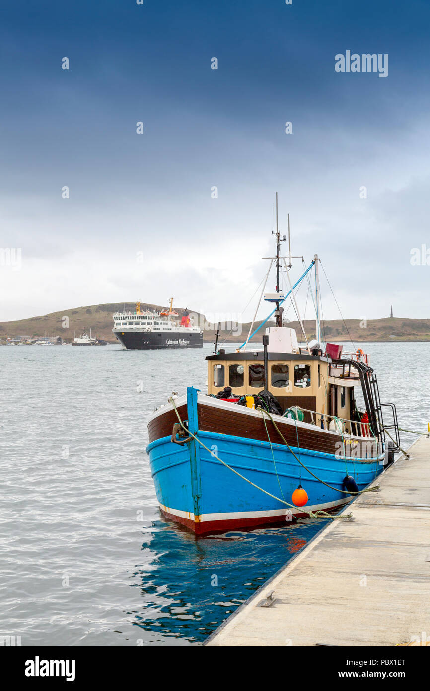A small fishing boat is moored near the North Pier as a CalMac outer islands ferry 'Isle of Lewis' arrives in Oban, Argyll and Bute, Scotland, UK Stock Photo