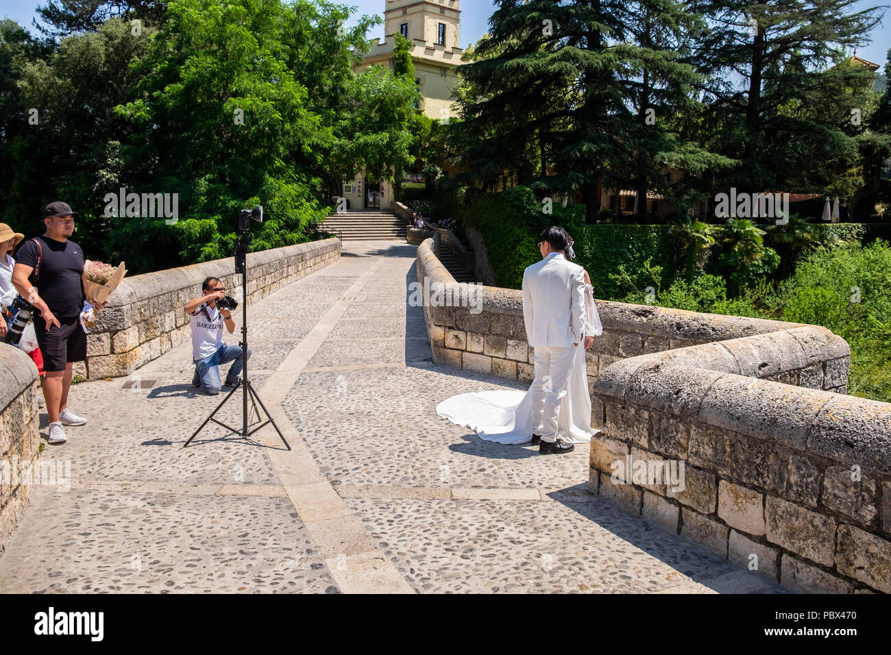 Wedding photographer at work photographing a newly wed couple on the Romanesque bridge over the river Fluvia in Besalu, garrotxa, Catalonia, Spain Stock Photo