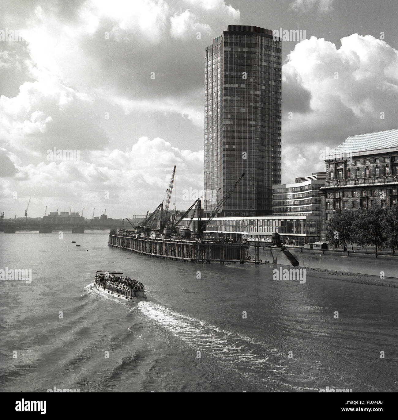 1960s, historical, a pleasure boat goes down the river Thames at the cleveland bridge landing stage or floating platform, beside a newly built modern high-rise office building  London, England, UK. The 60s saw the riverside of the Thames change for ever as wharves were developed into tower blocks and housing. Stock Photo