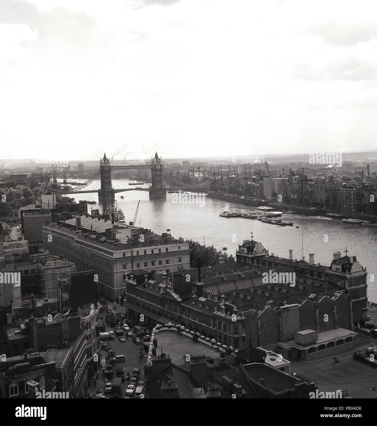 1950s, historical, a view down the river Thames looking south, with Tower Bridge in the distance, London, England, UK. At the bottom of the picture is the Billingsgate fish market at Lower Thames Street. At this time, the Thames was very much a working industrial river, as can be seen by the large number of loading or quay cranes at the different wharves where the ships would load and unload their cargo. Stock Photo
