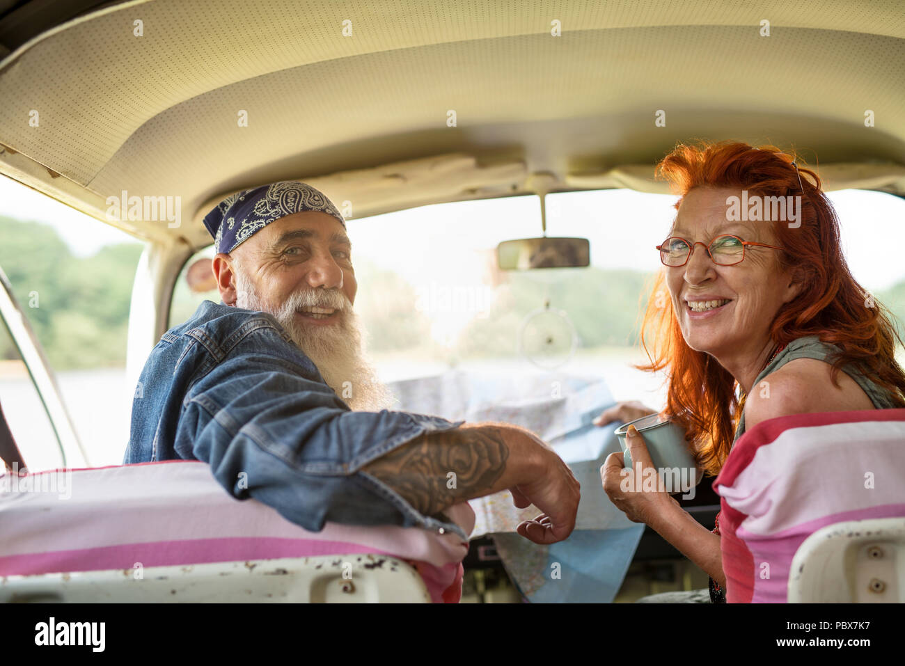 A hipster senior couple on vacation in a van, looking at camera Stock Photo