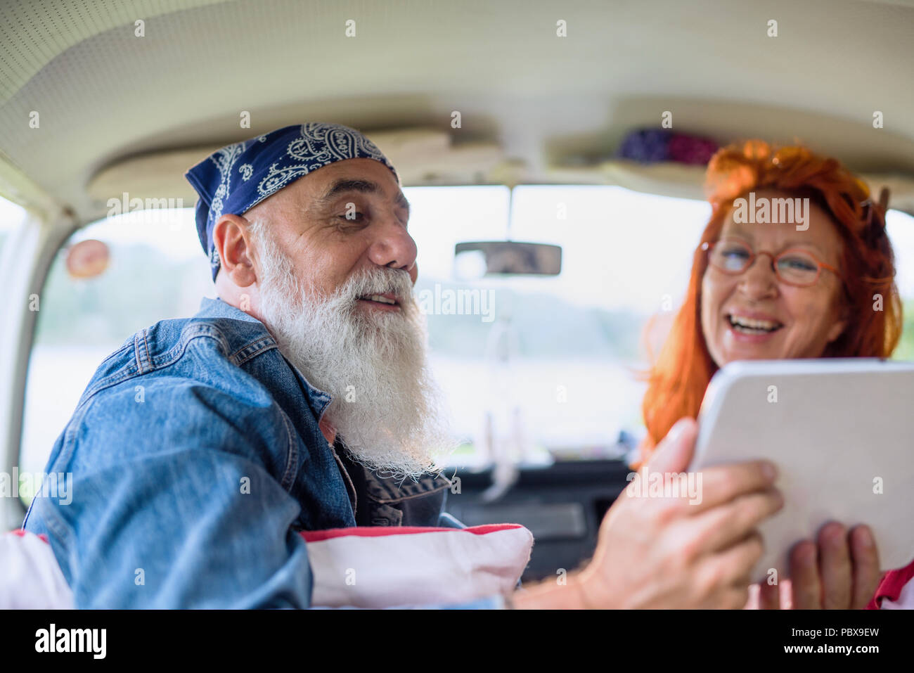 An old hipster couple sitting in a van, using a digital tablet Stock Photo