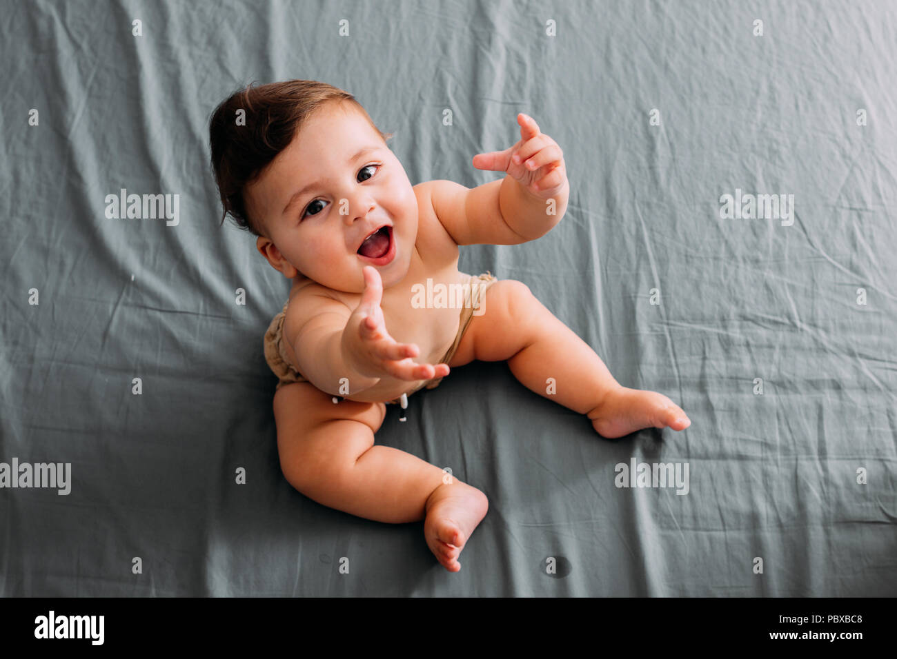 Top view of smiling baby sitting on the bed in the room wearing shorts Stock Photo