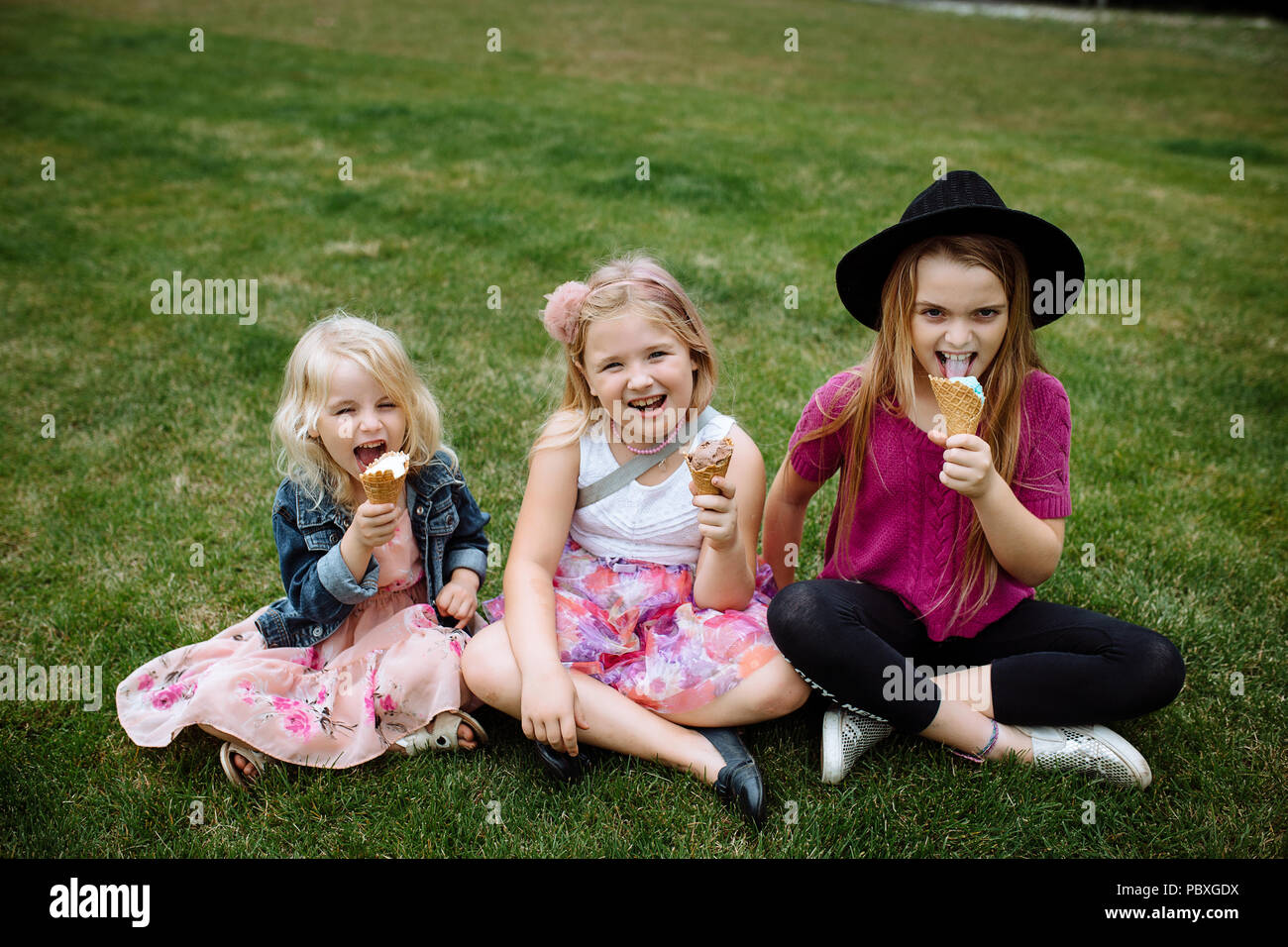 Happy smiling kids eating ice cream in the open air in the summer park. Three sisters Stock Photo