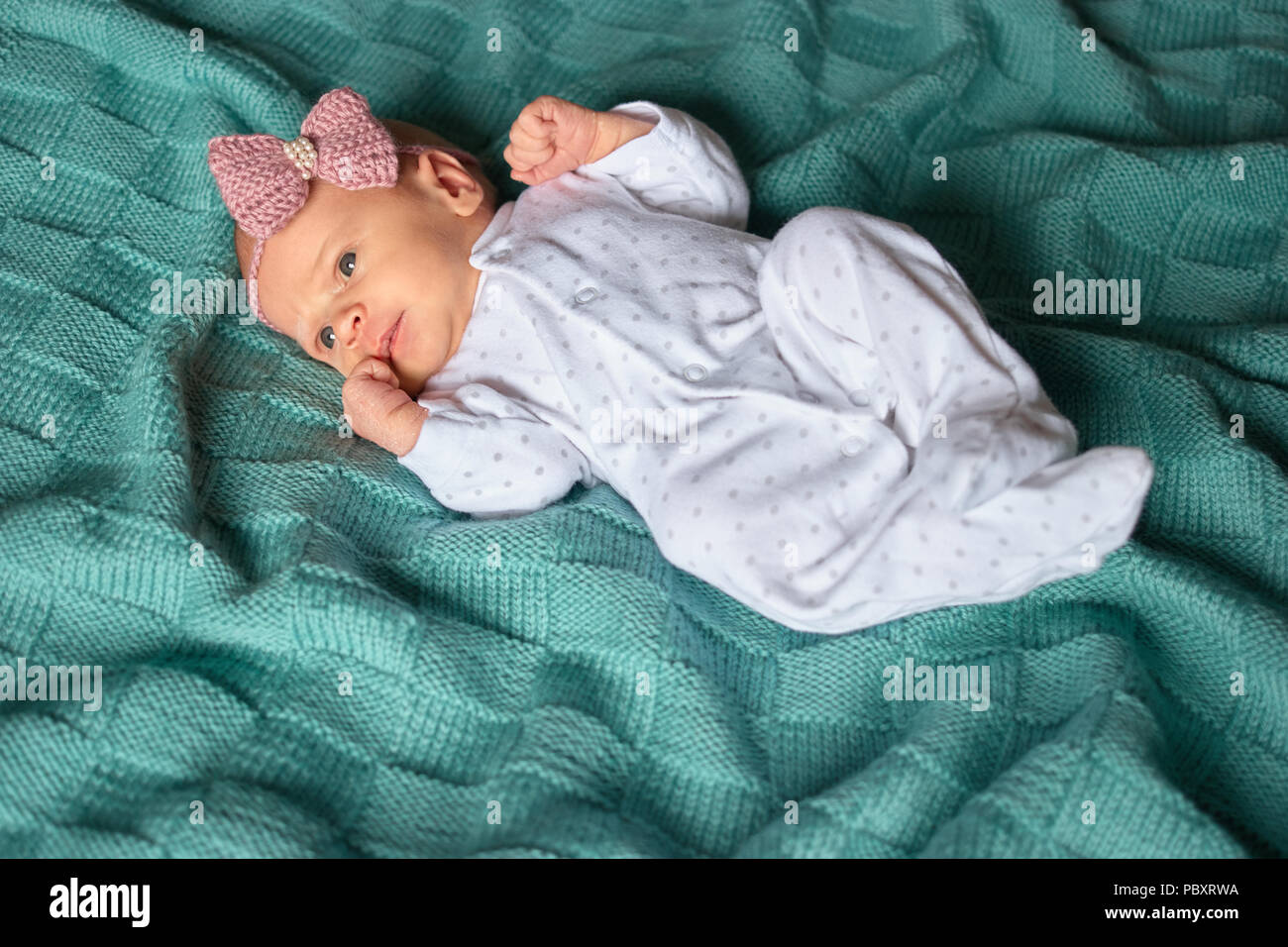 Newborn baby girl with bow in white footed pajamas. Top view