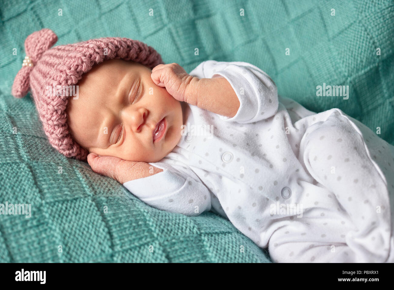 Baby girl lying on her back covering her ears. Newborn baby closes her