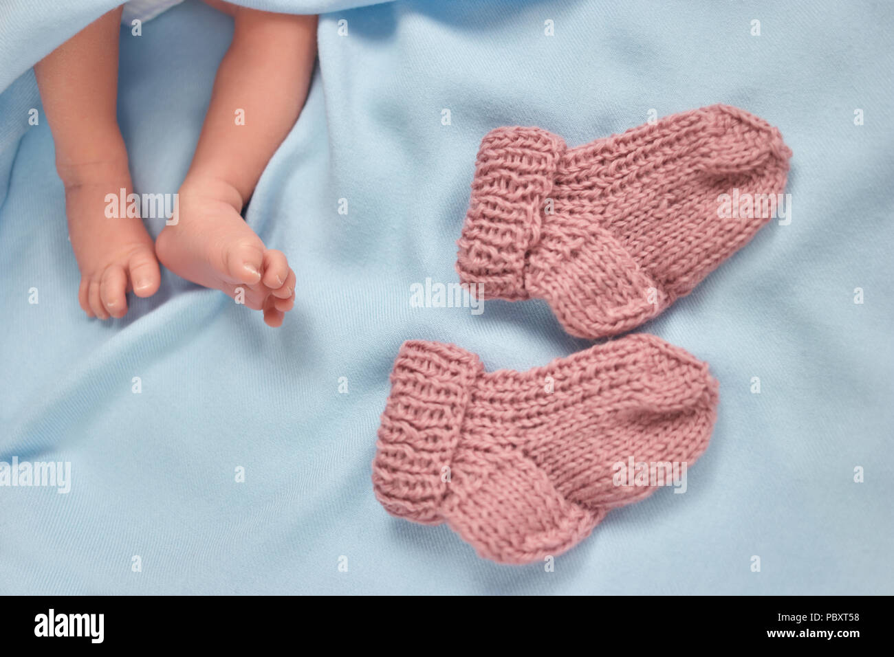 Tiny newborn baby feet and warm wool socks. Pair of knitted socks. Blue blanket. Stock Photo