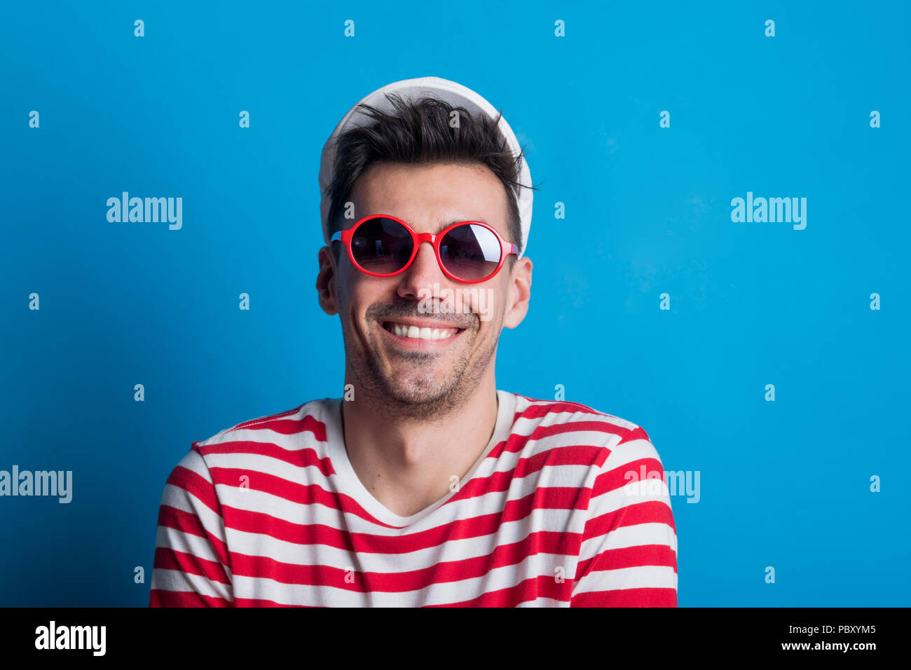 Portrait of a young man in a studio with sunglasses on a blue ...