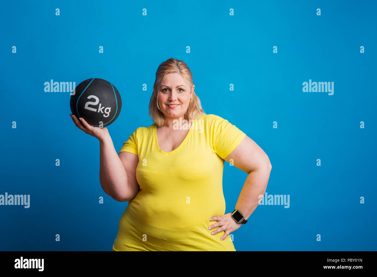 Portrait of a happy overweight woman holding a heavy ball in studio. Stock Photo