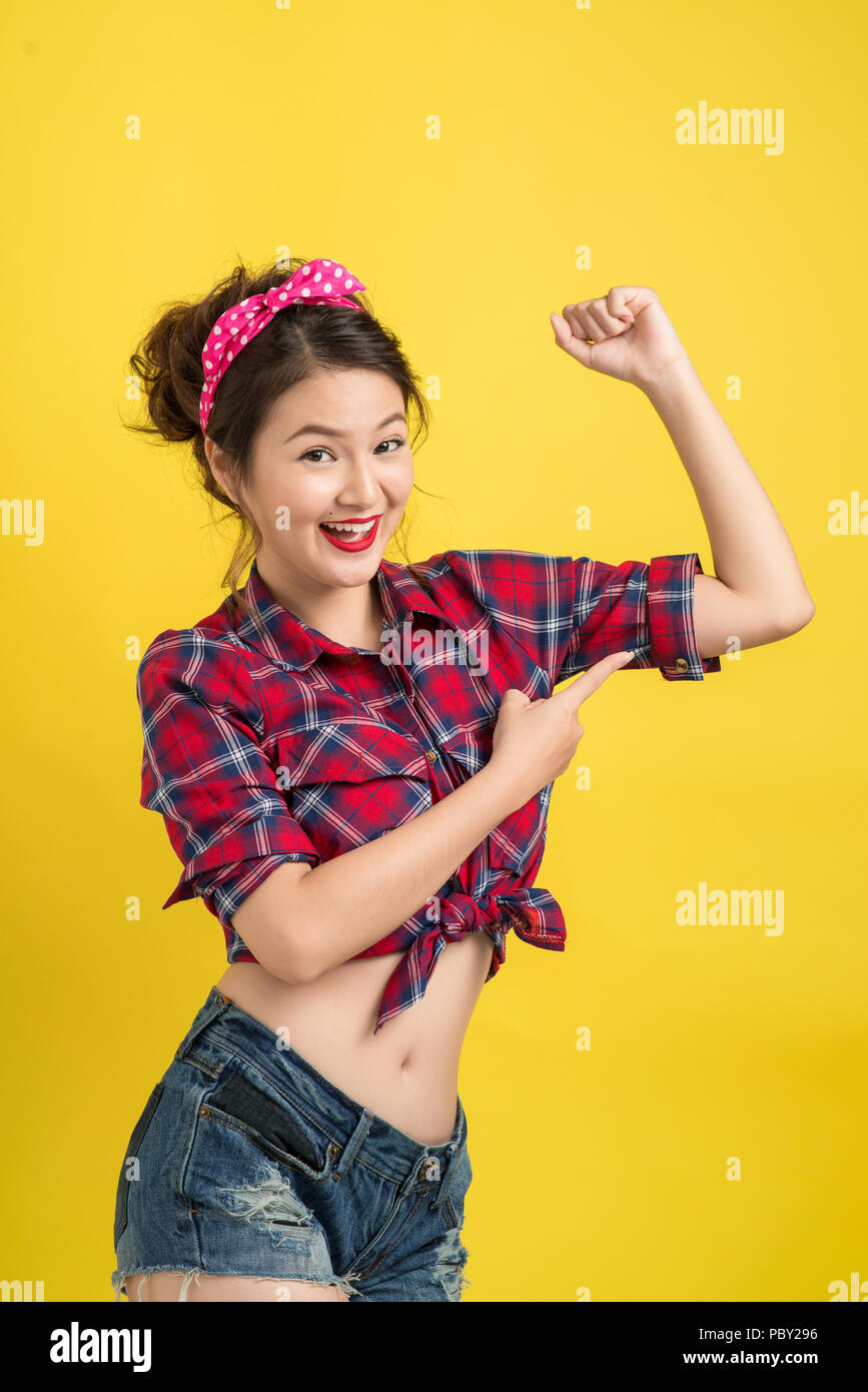 Young pin-up asian woman like classic We Can Do It poster over yellow background Stock Photo
