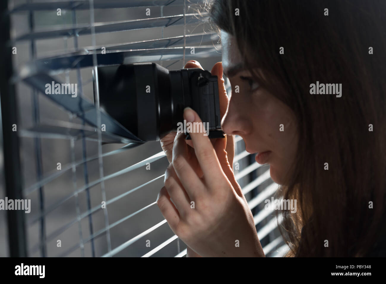 Young woman Paparazzi take a photo suspiciously from around a blinds  while using a camera. GDPR Concept Stock Photo