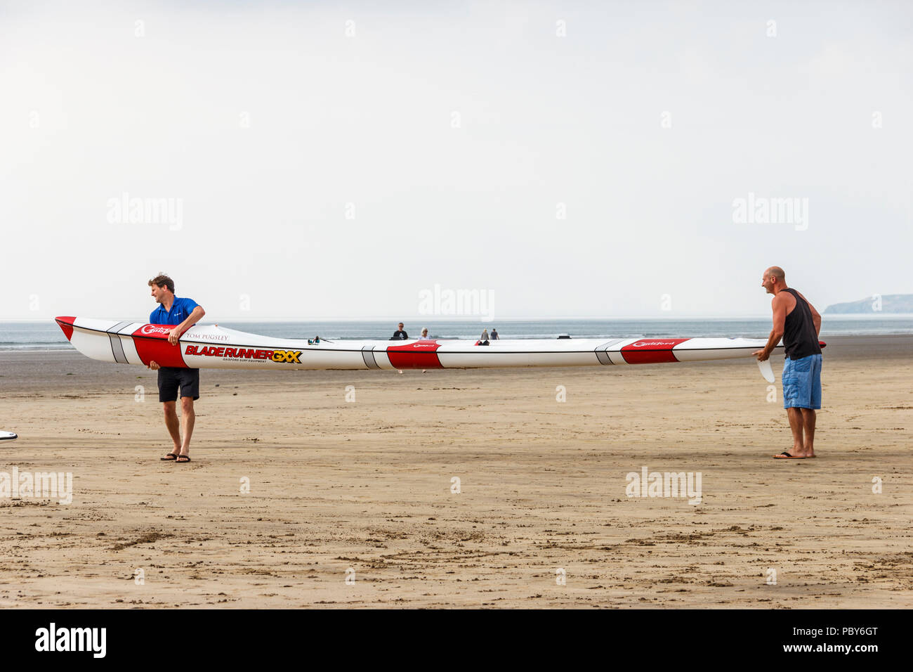 Two men carrying a Gaisford Bladerunner double surf ski on the beach at Westward Ho!, Devon, UK Stock Photo
