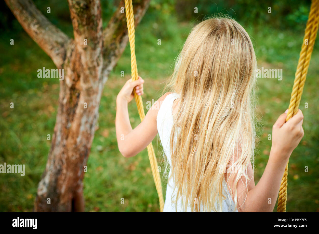A child cute girl swinging on a rope ladder in summer in the garden Stock Photo