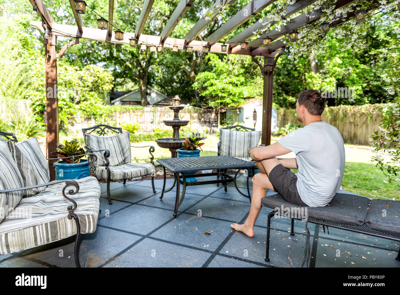 Young Man Sitting On Patio Lounge Chair In Outdoor Spring Flower