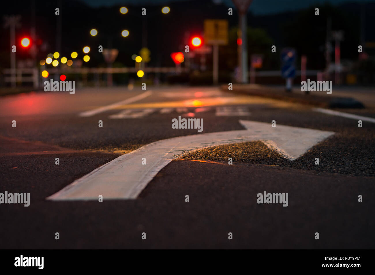 Low angle view of a right turn arrow painted on the road with a railway crossing in the background Stock Photo