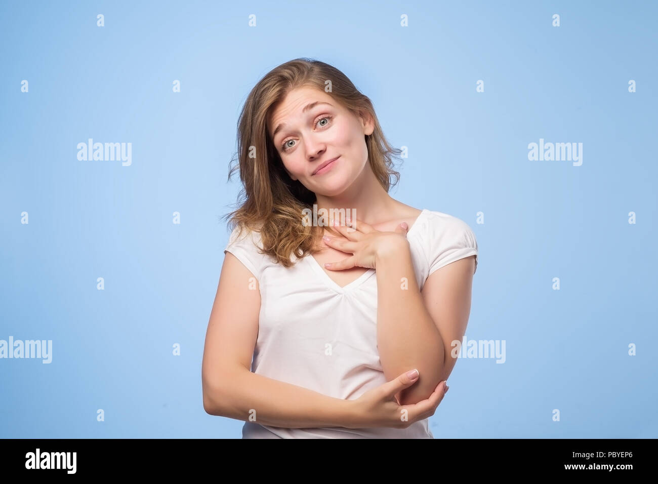 Pleased Caucasian woman wearing white top smiling broadly and keeping hand on her cheek, glad to receive compliments Stock Photo